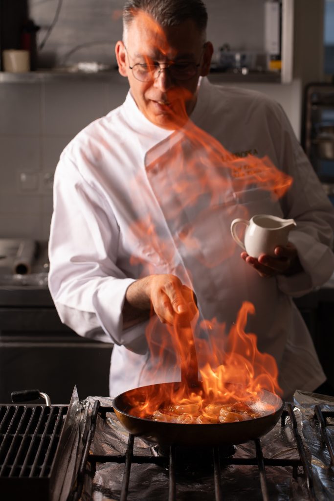 Szef kuchni flambiruje danie na patelni w otwartej kuchni restauracji La Tropea