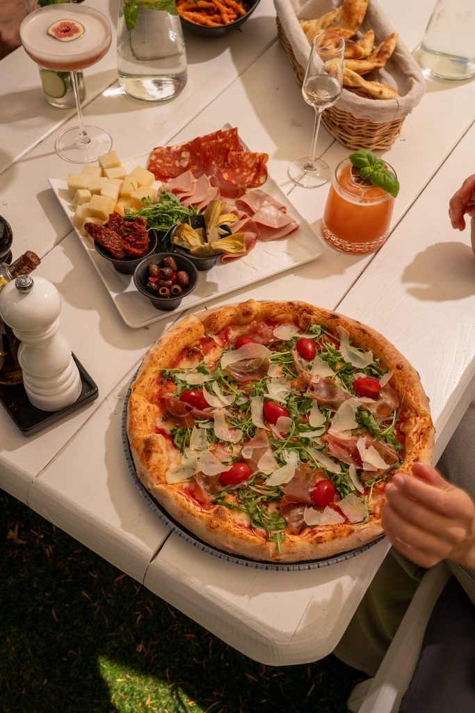Pizza z rukolą i prosciutto oraz deska wędlin na stole w ogródku restauracji La Tropea