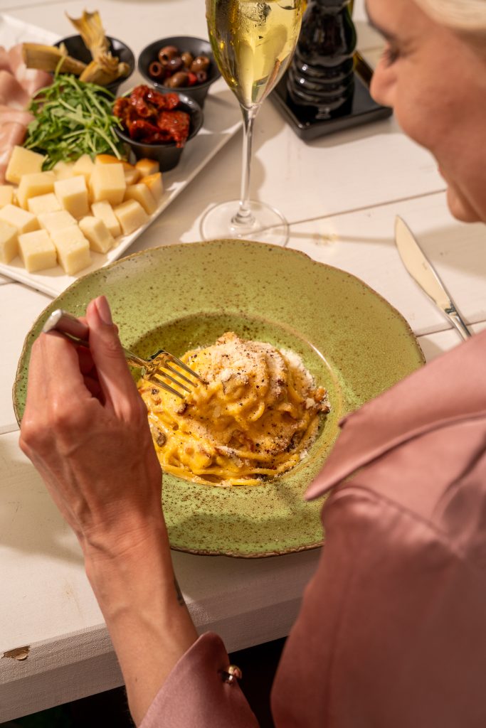 Kremowe spaghetti cacio e pepe na zielonym talerzu z kieliszkiem białego wina