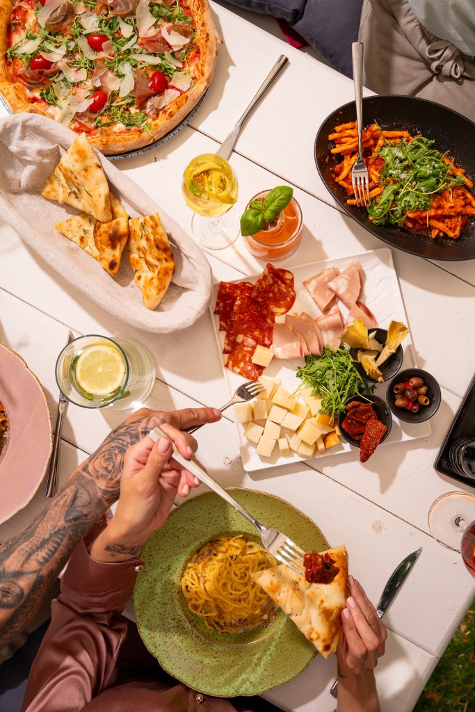 Stół pełen pizzy, makaronu i antipasti widziany z góry podczas wspólnego posiłku