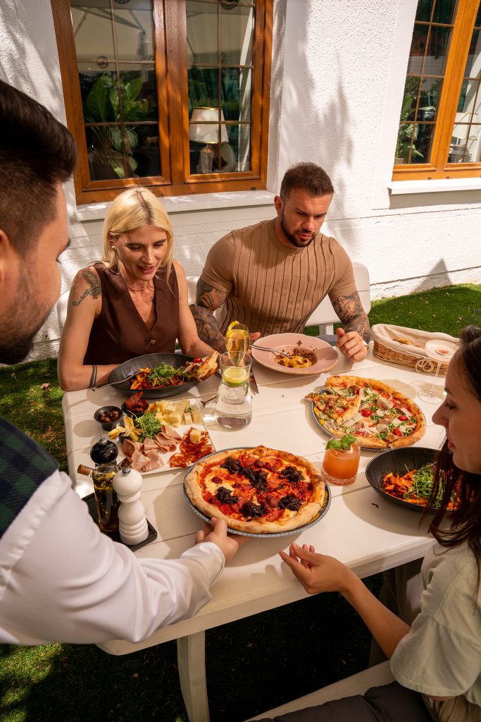 Grupa gości je pizzę i makaron przy stole w ogródku restauracji La Tropea