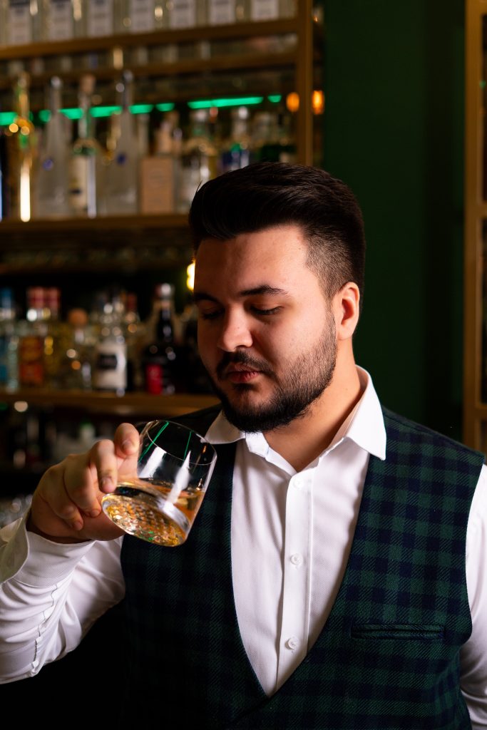 Barman w kraciastej kamizelce ocenia drink przy barze restauracji La Tropea